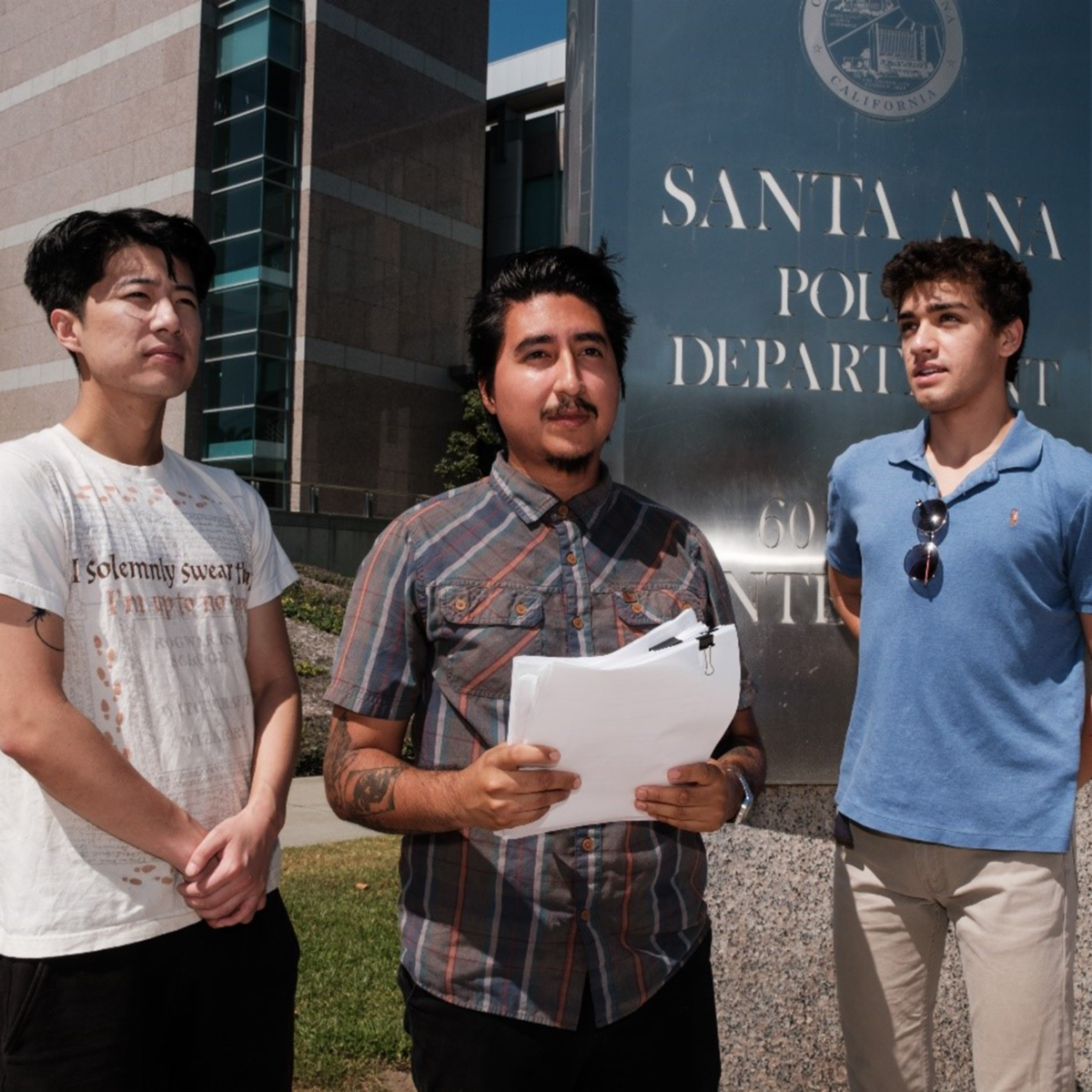 Three IPAT students standing in front of Santa Ana Police Department with one holding a packet of documents.