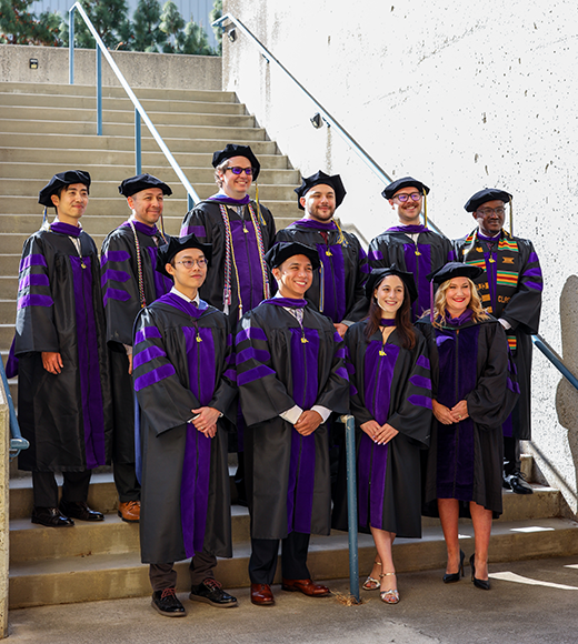 Grad Tax students stand in regalia at commencement with administrator Natascha Fastabend